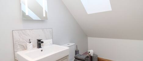 A modern bathroom with a skylight, a white sink, a toilet, and a mirror above the sink.