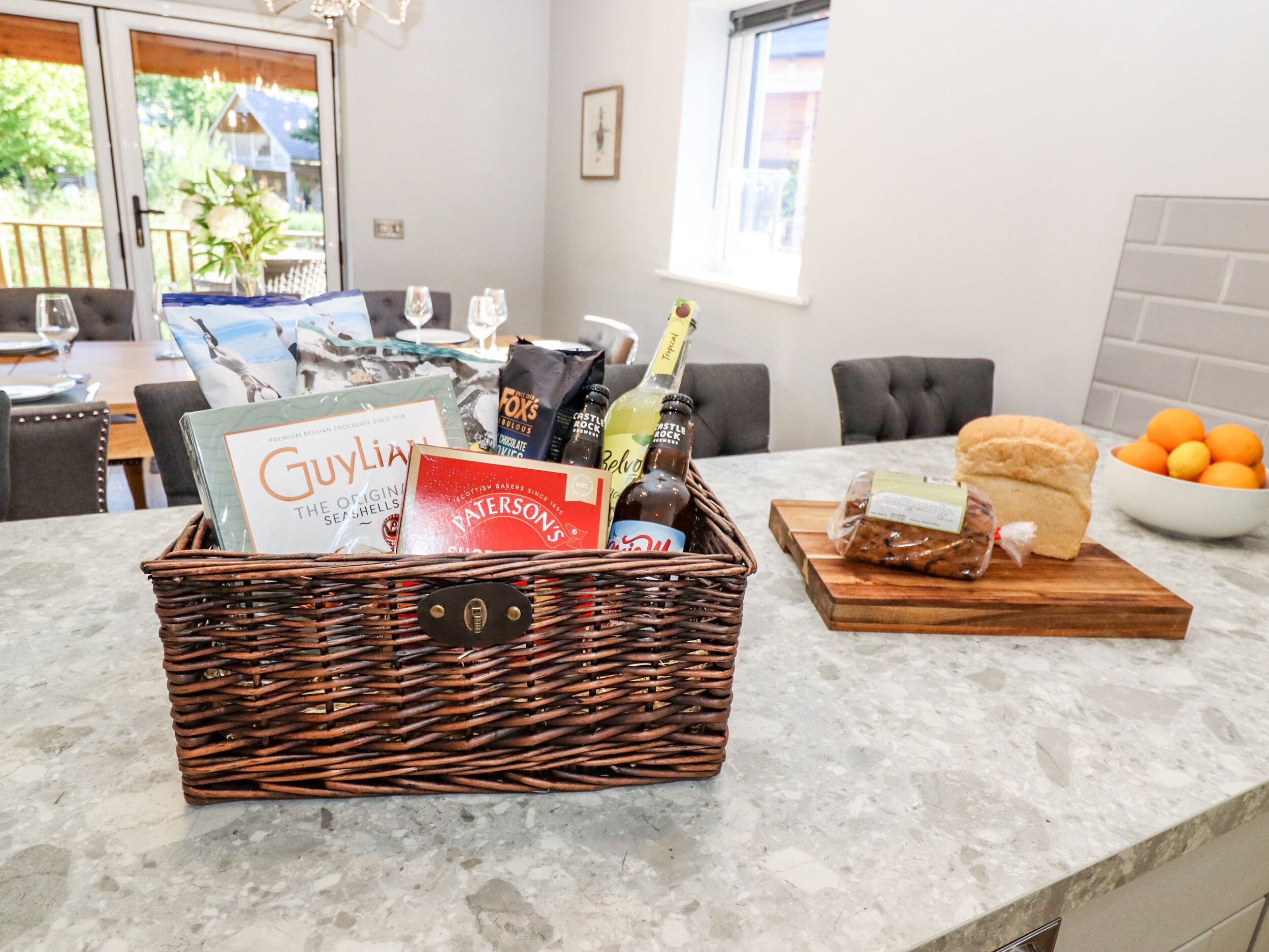 A kitchen counter with a wicker basket containing chocolate bars, a bottle of champagne, and a loaf of bread.