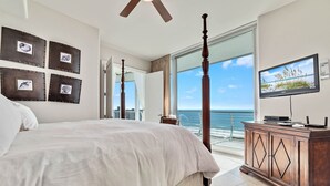Ein Schlafzimmer mit einem großen Bett, einem Fernseher, einer Holzkommode und einem Balkon mit Meerblick.