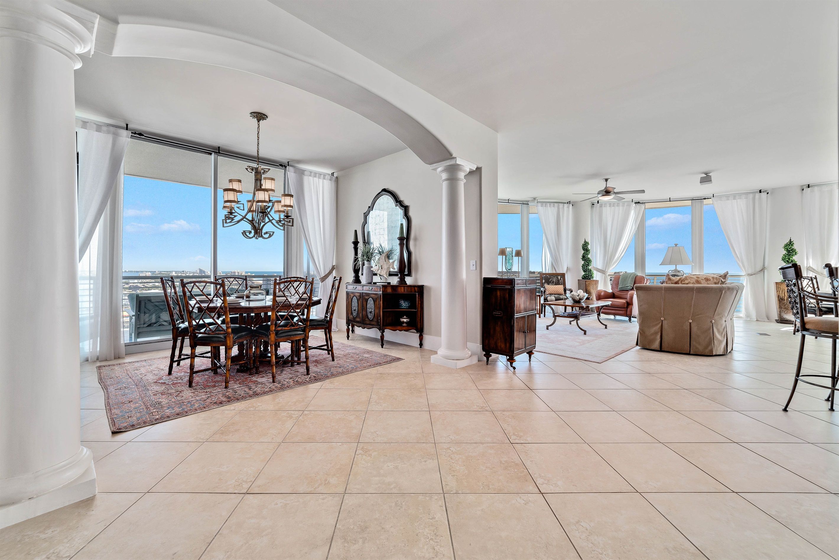 A spacious living area with a dining set, a large mirror, and a view of the cityscape through large windows.