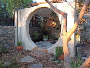 Une structure circulaire formant un jardin, avec un mur en pierre, des plantes en pot et un chemin en pierre.