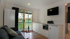 Enjoy a homey atmosphere in this cozy space, featuring a kitchenette with a flat-screen TV, a small dining area, and a balcony with sliding glass door.