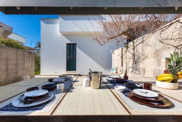 An outdoor dining area with a modern setting, including a table set with plates, bowls, and a fruit bowl.