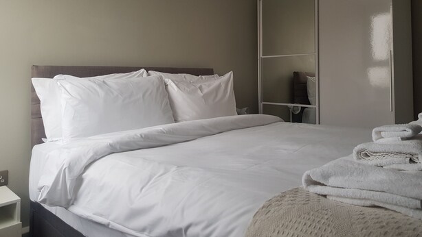 Un lit bien fait, avec du linge de lit blanc, une tête de lit en bois et une grande armoire aux portes miroir.