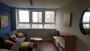 Un salon moderne avec un canapé gris, des coussins jaunes, une petite table ronde et un meuble en bois.