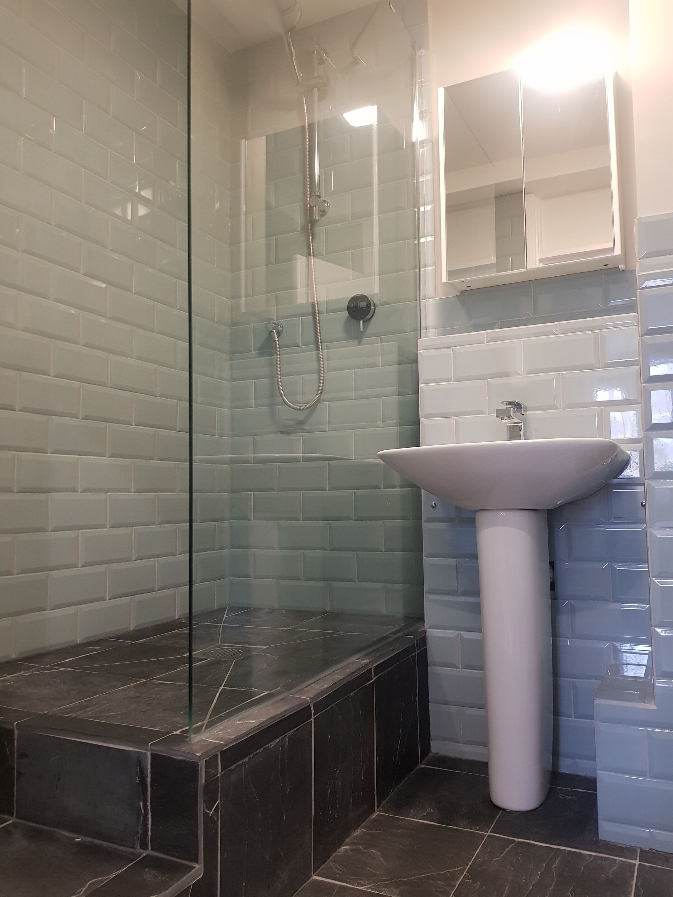 A bathroom with a glass-enclosed shower, a white pedestal sink, and tiled walls.