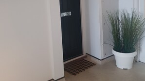 Un couloir avec une porte noire portant le numéro 43, un mur blanc et une plante en pot.