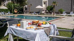 Un coin petit-déjeuner aménagé au bord de la piscine, avec une table, des chaises et la piscine en arrière-plan.