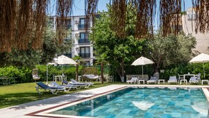 Une piscine entourée de chaises longues et de parasols, avec de la verdure tout autour et un bâtiment en arrière-plan.
