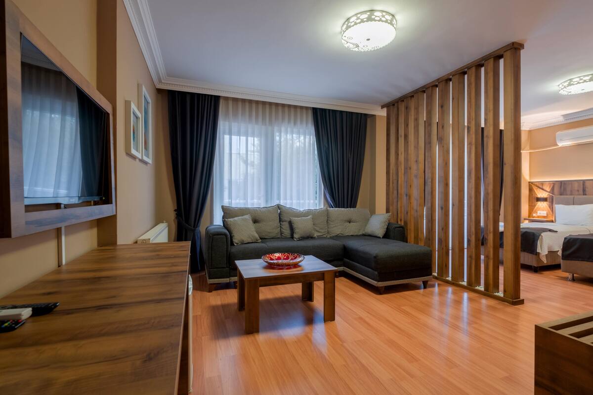 A modern living room with a wooden floor, a sectional sofa, a coffee table, and a TV mounted on the wall.