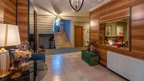 Un intérieur moderne avec un escalier, des lambris en bois, une petite table d’appoint verte et un miroir qui reflète la pièce.