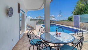 Area piscina con tavolo rotondo, sedie e una bottiglia di vino rosso.