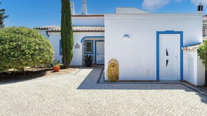 Un edificio bianco con una porta blu e un piccolo giardino con vasi di piante e un albero alto.
