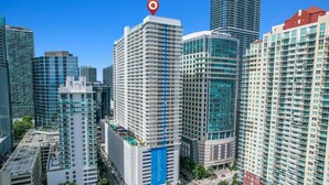 Um edifício alto com uma faixa vertical azul destacada, rodeado por outros edifícios altos.