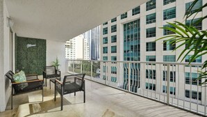 Uma varanda com área de estar, uma parede verde com uma placa, e vista para edifícios altos.