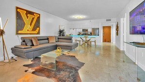 Uma sala de estar moderna com um sofá seccional, uma mesa de centro de vidro e um grande letreiro neon 'LV'.