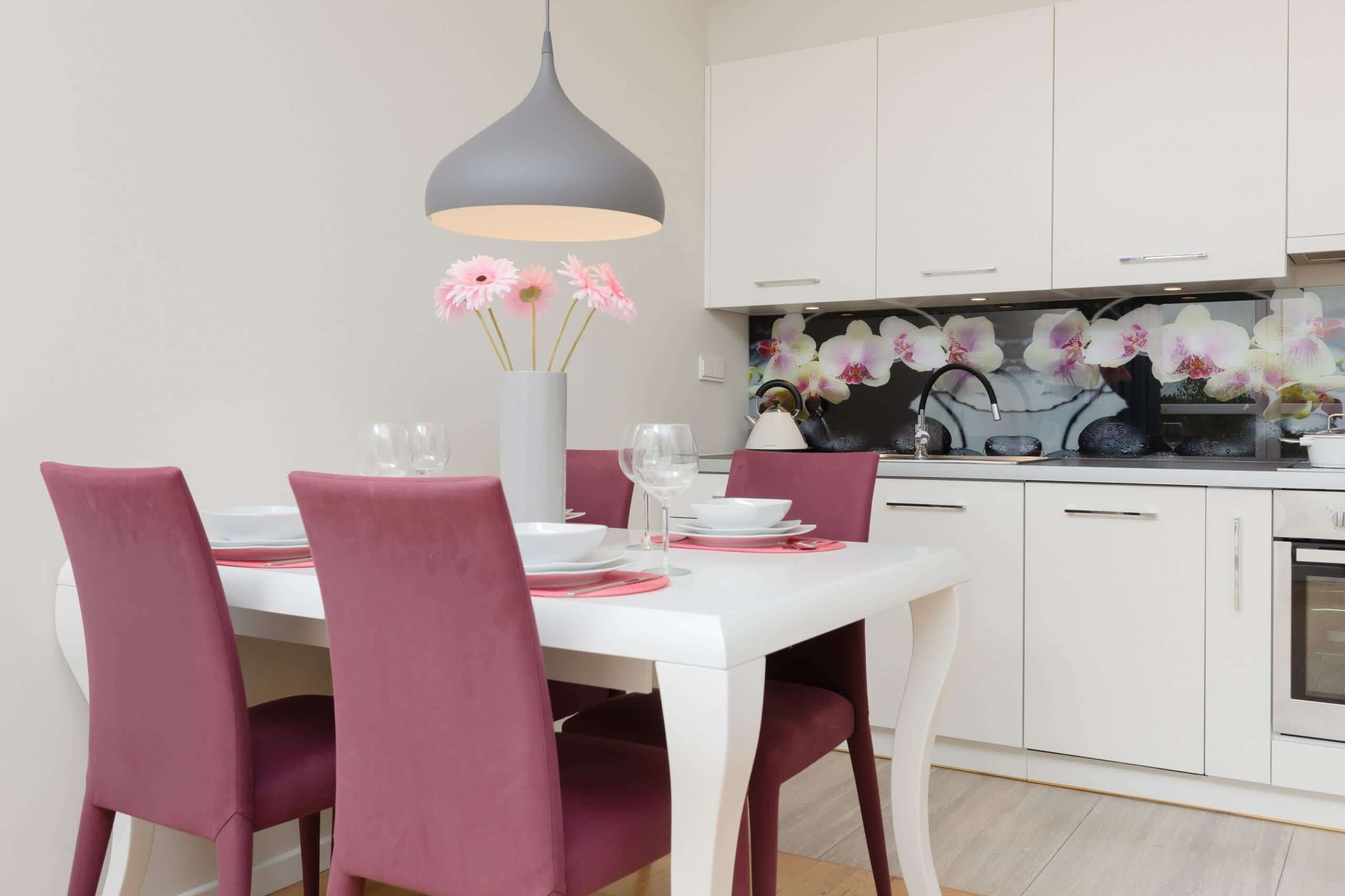 A modern kitchen with white cabinets, a white countertop, and a pendant light above the dining table.