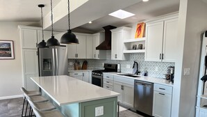 A modern kitchen with white cabinets, a central island with bar stools, stainless steel appliances, and a patterned backsplash.