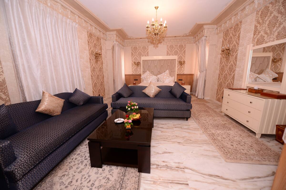 A spacious bedroom with a large bed, two sofas, a coffee table, and a dresser.