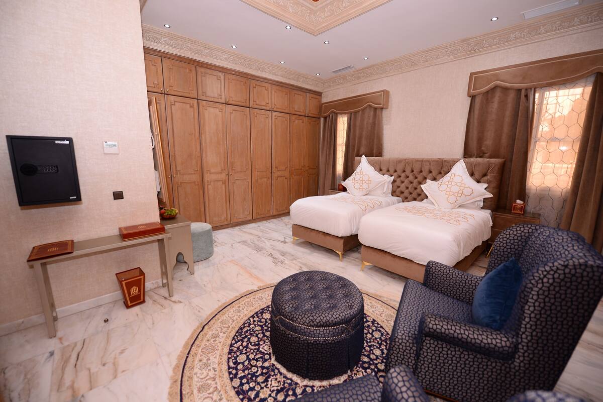 A bedroom with a large bed, a TV, wooden cabinets, and a round ottoman.