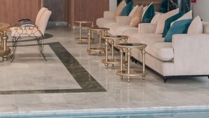 A modern indoor pool area with a white sofa set, gold-framed tables, and a marble floor. - THE WHITE PALACE RABAT (Rabat)