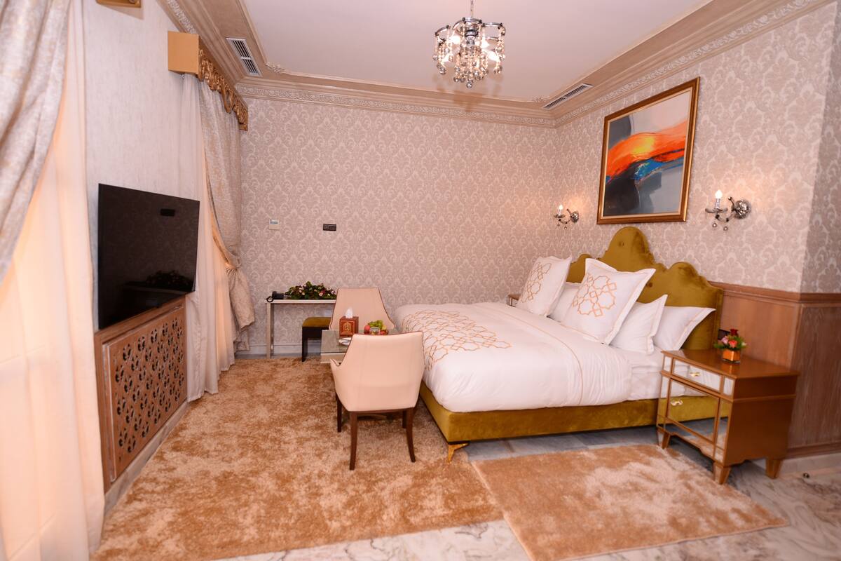 A bedroom with a large bed, a TV, a desk, and a chandelier.