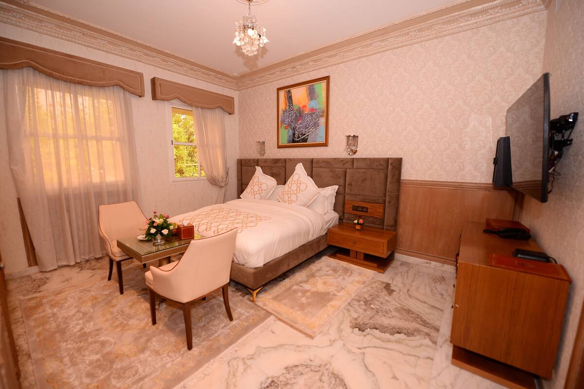 A bedroom with a bed, a desk, a chair, a TV, and a nightstand.