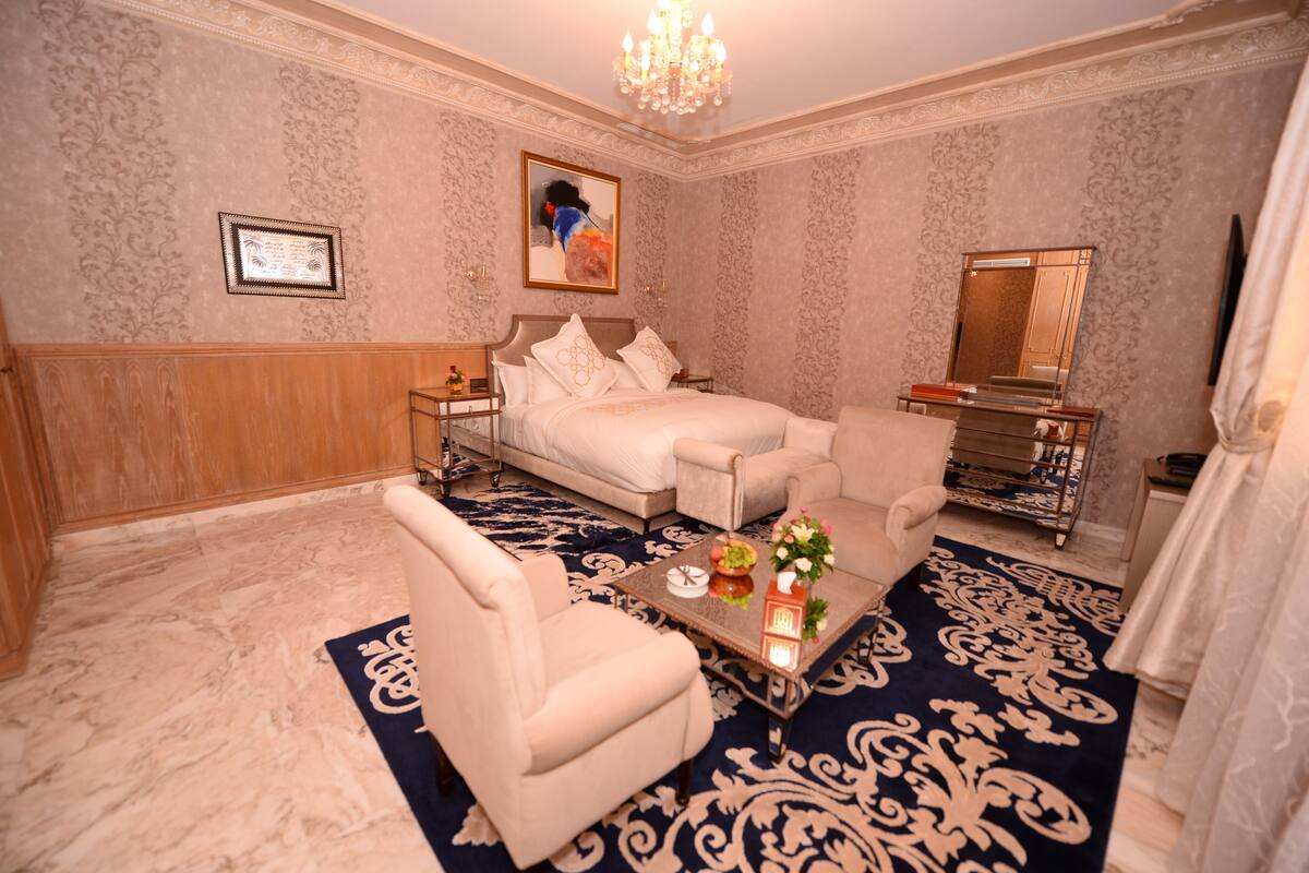 A hotel room with a bed, a sofa, a coffee table, a chair, a mirror, and a chandelier.