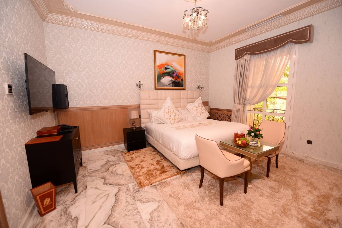 A bedroom with a bed, bedside table, TV, and a desk with a chair.