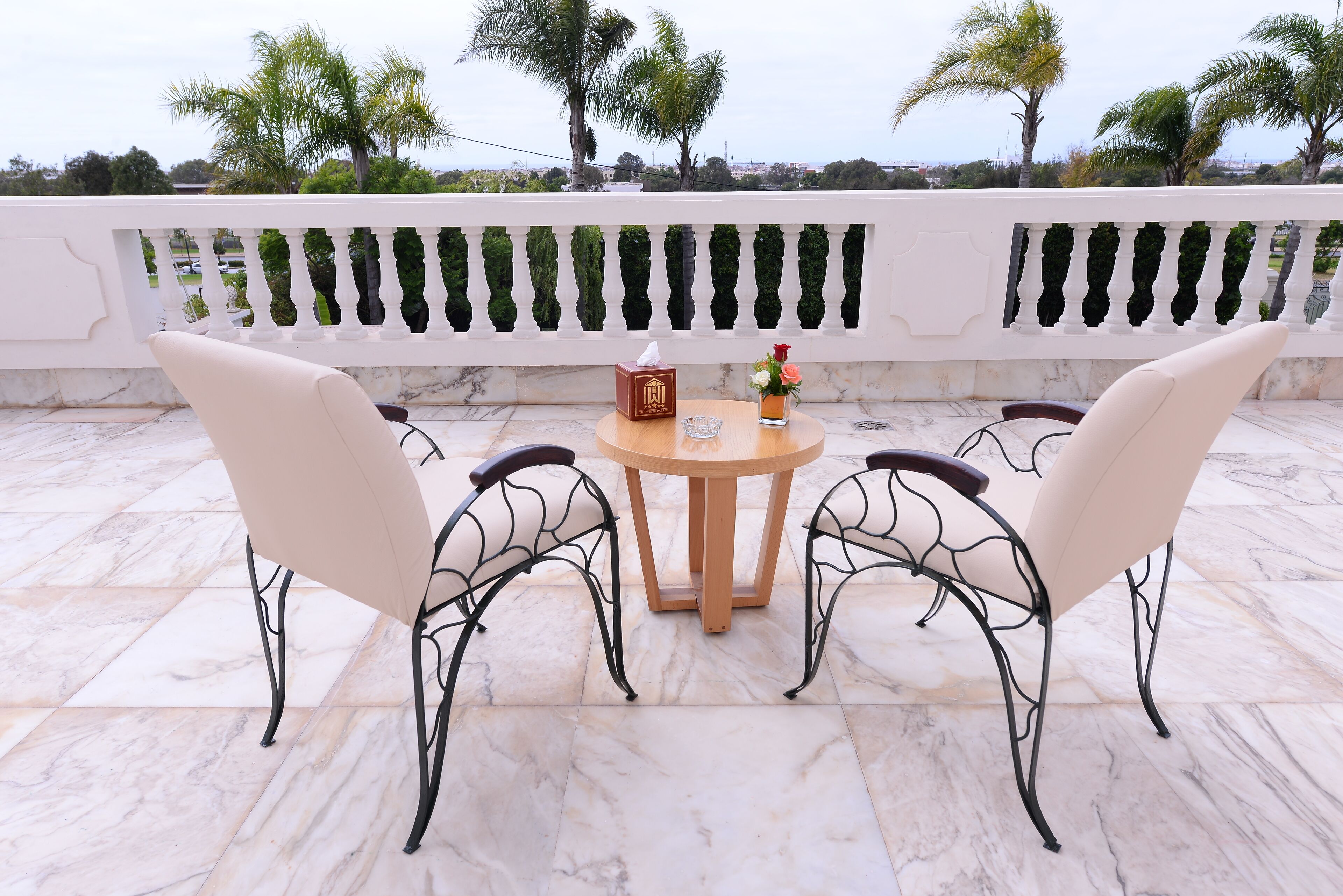 Une terrasse avec deux chaises beiges, une table en bois et un vase rempli de fleurs.