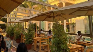 An outdoor seating area with wooden furniture and potted plants, overlooking a building with classical architecture. - THE WHITE PALACE RABAT (Rabat)