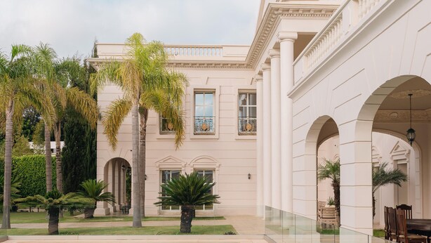 A pool area with a clear view of the pool, palm trees, and a building with arched walkways. - THE WHITE PALACE RABAT (Rabat)