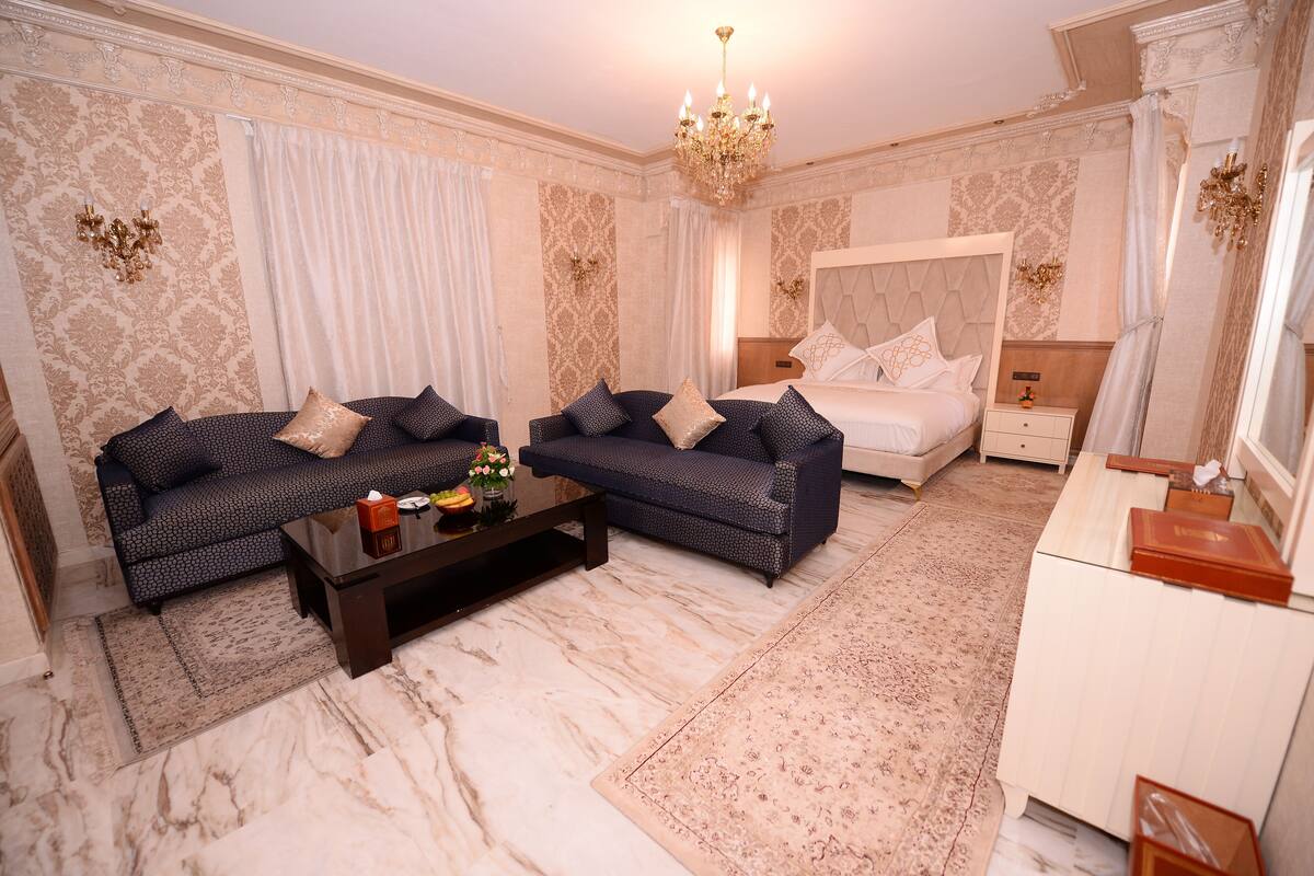 A hotel room with a large bed, two sofas, a coffee table, and a desk.