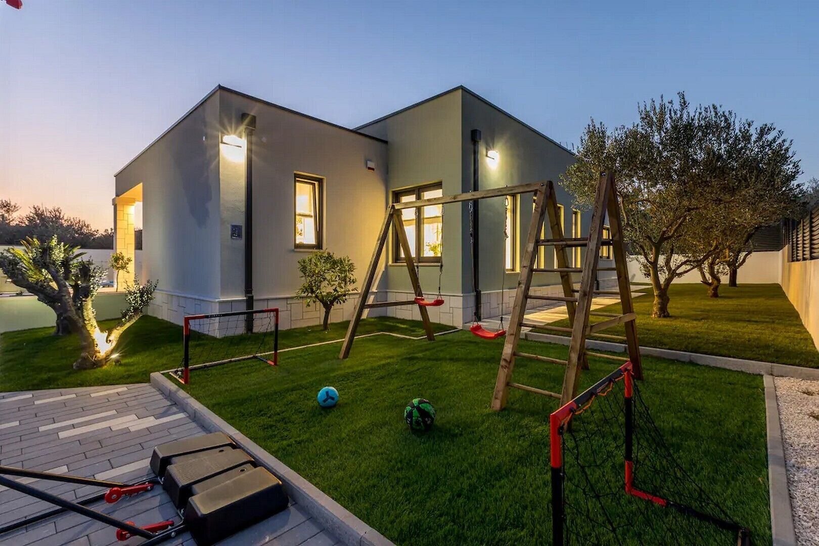 A modern house with a well-maintained lawn, a swing set, and a basketball hoop.