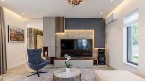 Una sala de estar moderna con un televisor de pantalla plana grande, un sillón azul, un sofá blanco y una mesa de centro redonda.