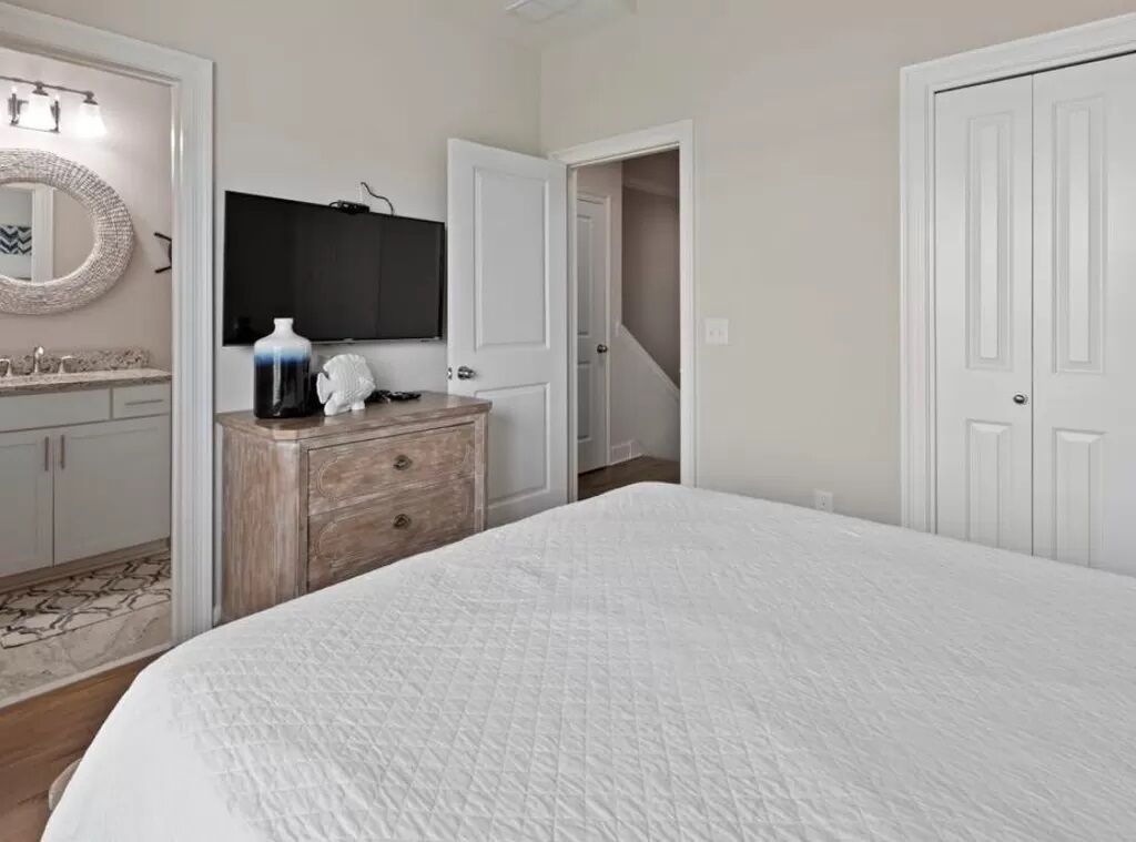 Une chambre à coucher avec un grand lit, une commode, un miroir, une télévision et une porte donnant sur un placard.
