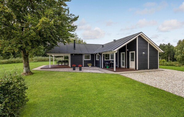 Enjoy a serene setting surrounded by lush greenery and trees on this two-story house's covered patio with outdoor seating.
