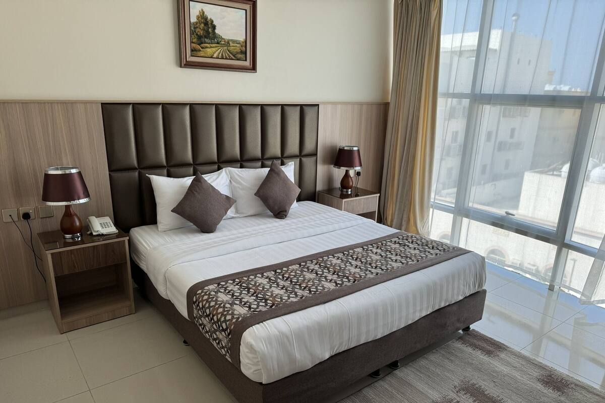 Quarto de hotel moderno com uma cama grande, duas mesas de cabeceira, uma cabeceira e vista através de uma janela ampla.