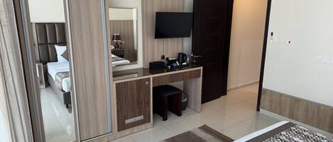 Habitación de hotel con cama, escritorio con televisor de pantalla plana, espejo, armario y puerta de baño.