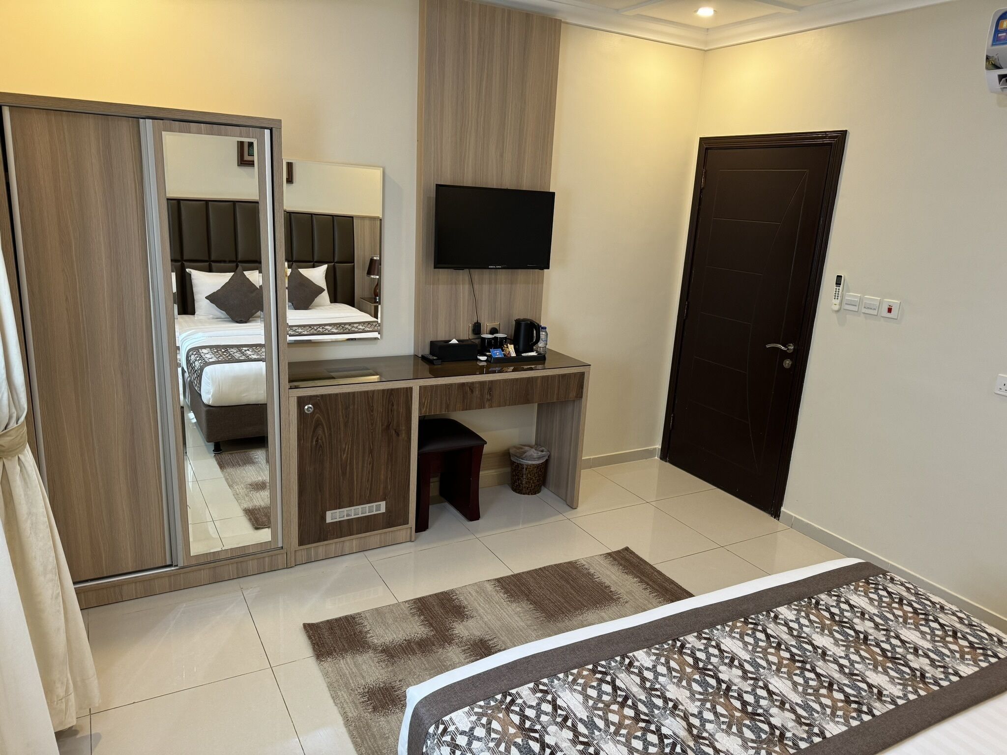 Habitación de hotel con cama, escritorio con computadora, televisión, armario y puerta.