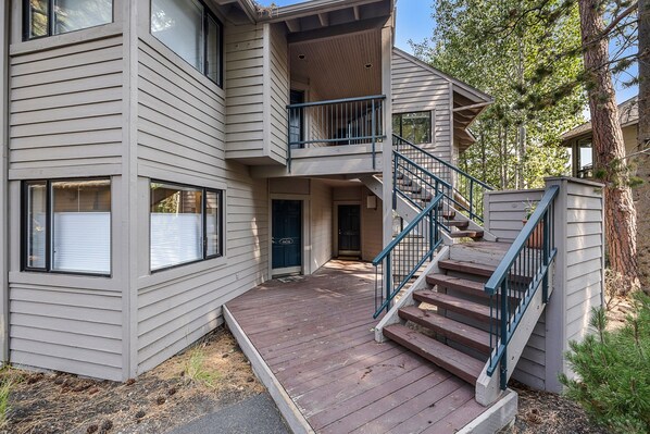 Un bâtiment à deux étages doté d’une terrasse en bois et d’un escalier bleu menant à un balcon.