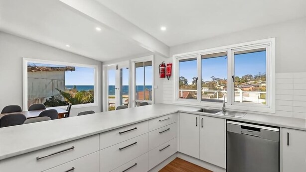 Una cocina moderna con armarios blancos, lavavajillas y ventanas amplias con vista al mar.