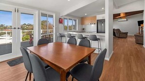 Una cocina moderna con una isla central, un comedor con mesa y sillas de madera, y una sala de estar con sofá y televisor.