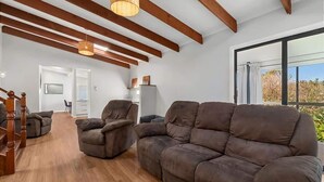 Una sala de estar moderna con un sofá de cuero marrón, una escalera de madera y un amplio ventanal con vistas.