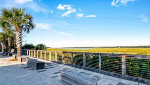 A paved walkway with benches, palm trees, and a view of a marshy landscape. - 2 bedroom villa just steps to the pool with a fantastic lagoon view! (Hilton Head Island)