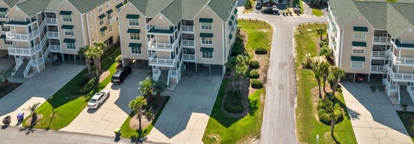 A multi-story hotel with balconies, a central courtyard, and a parking area. - CottageVacations4u "The Great Escape"-ocean view villa-pool club-direct beach access (Ocean Isle Beach)