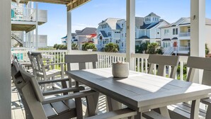 A covered outdoor seating area with a table and chairs, overlooking a row of beach houses. - CottageVacations4u "The Great Escape"-ocean view villa-pool club-direct beach access (Ocean Isle Beach)