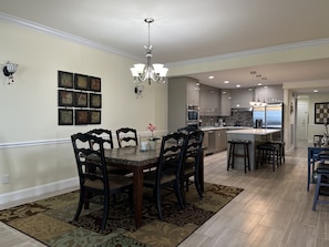 A spacious dining area with a large table and chairs, a chandelier, and a kitchen in the background. - BEACHFRONT Open Concept Corner Unit with Direct Ocean Views! (Wildwood)