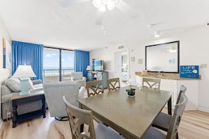 A dining area with a table and chairs, a sofa, a TV, and a view of the ocean.