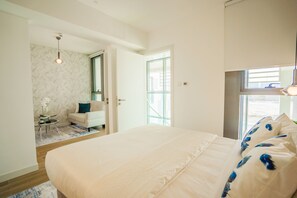 A bedroom with a large bed, a small seating area with a chair and table, and a window with a view. - Nasma Luxury Stays - Al Raha Lofts 2 (Abu Dhabi)